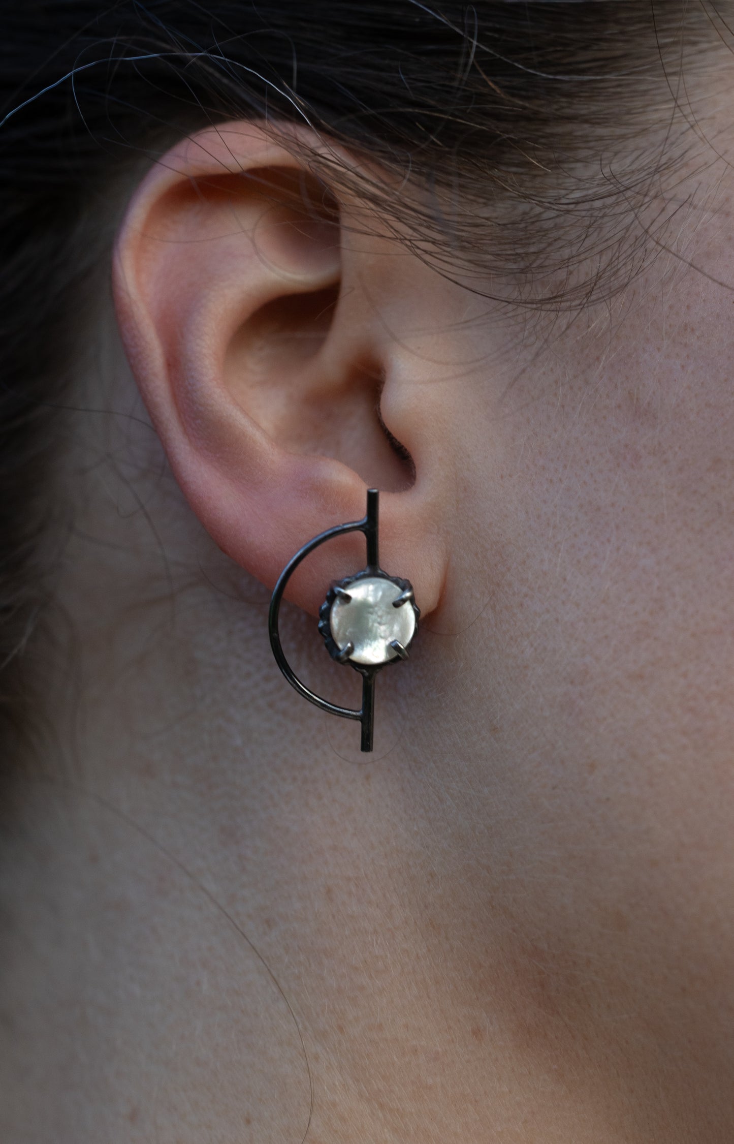 Close-up of an ear wearing a unique earring with a central gemstone by Alice Scott
