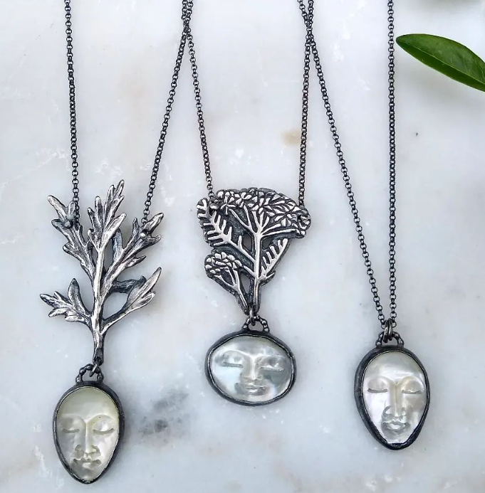 silver necklaceswith carved mother of pearl moon face and blackened silver yarrow and mugwort design on a marble background by Alice Scott