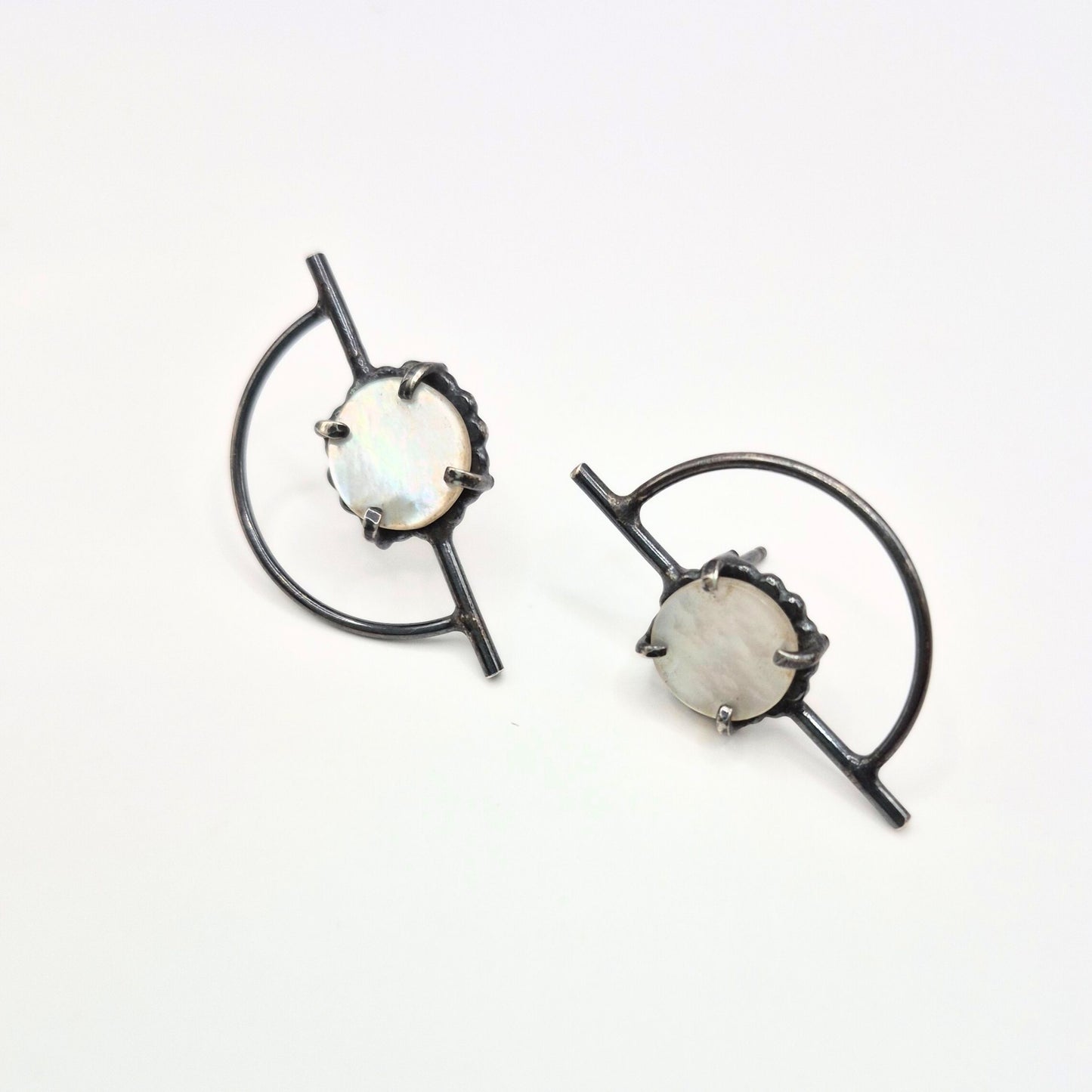 A pair of Orbit posts earrings with mother of pearl, featuring a geometric design with black silver posts and white-colored mother of pearl circles by Alice Scott