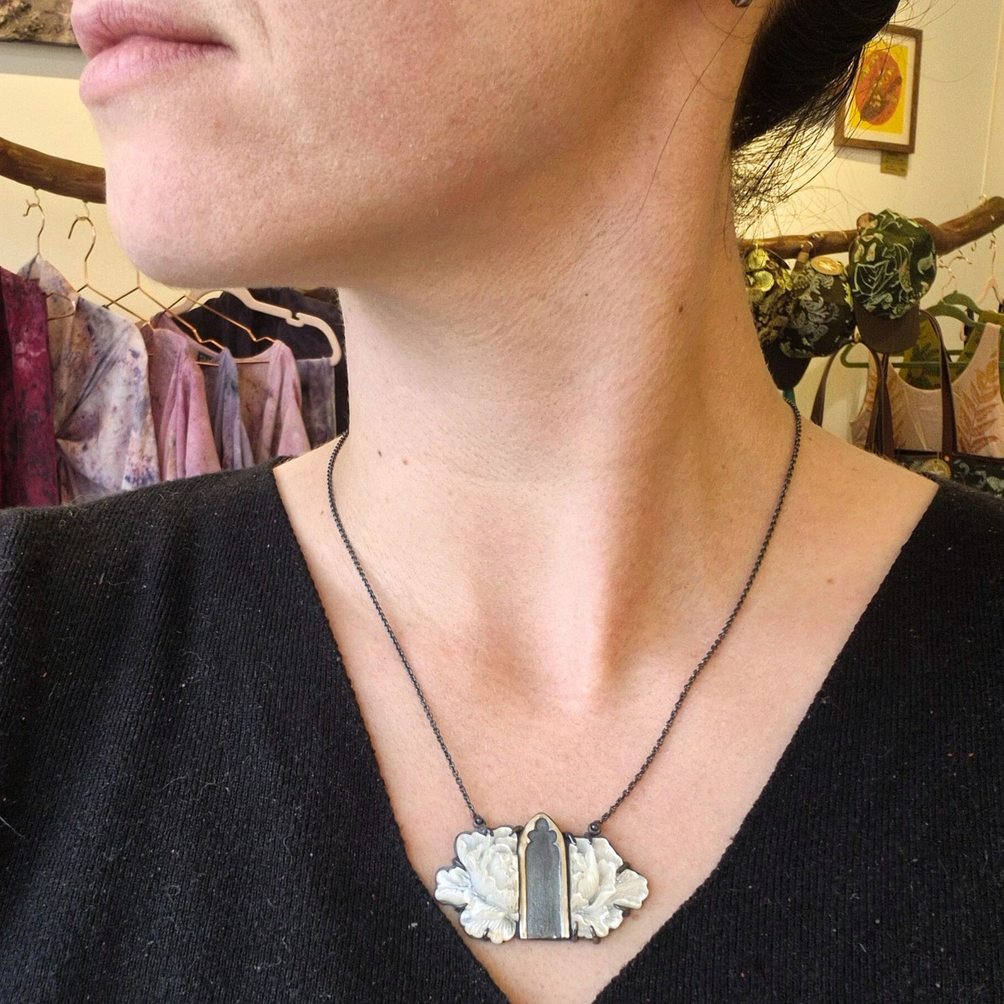A silver necklace with a mother of pearl flower design and Gothic archway cutouts, being worn on a woman profile by Alice Scott