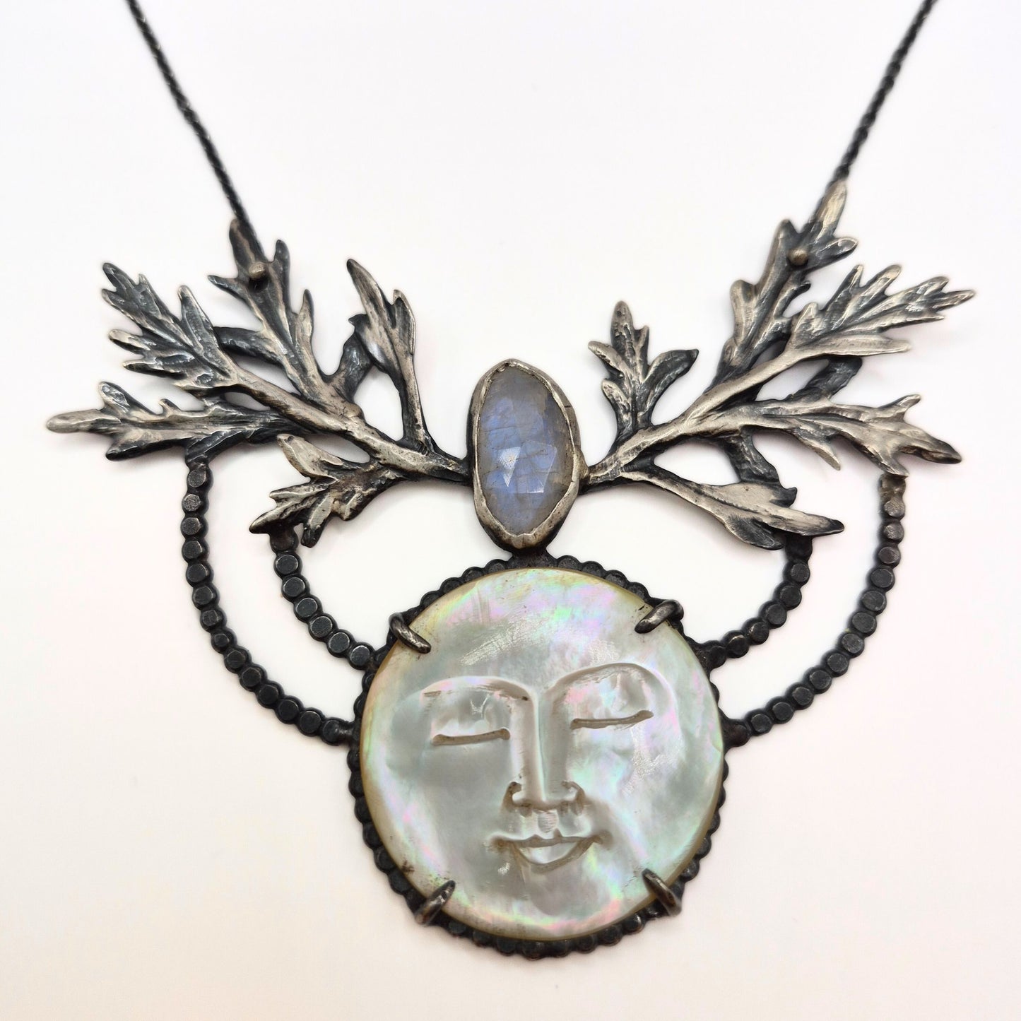 Necklace with leaf design and face pendant on a white background with mother of pearl, silver, and moonstone by Alice Scott