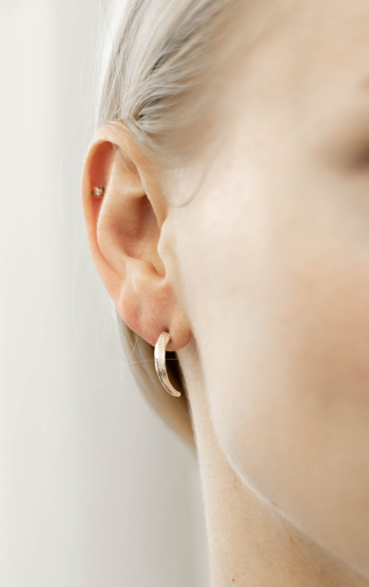A pair of silver earrings shaped like claws, displayed on a model ear by Alice Scott