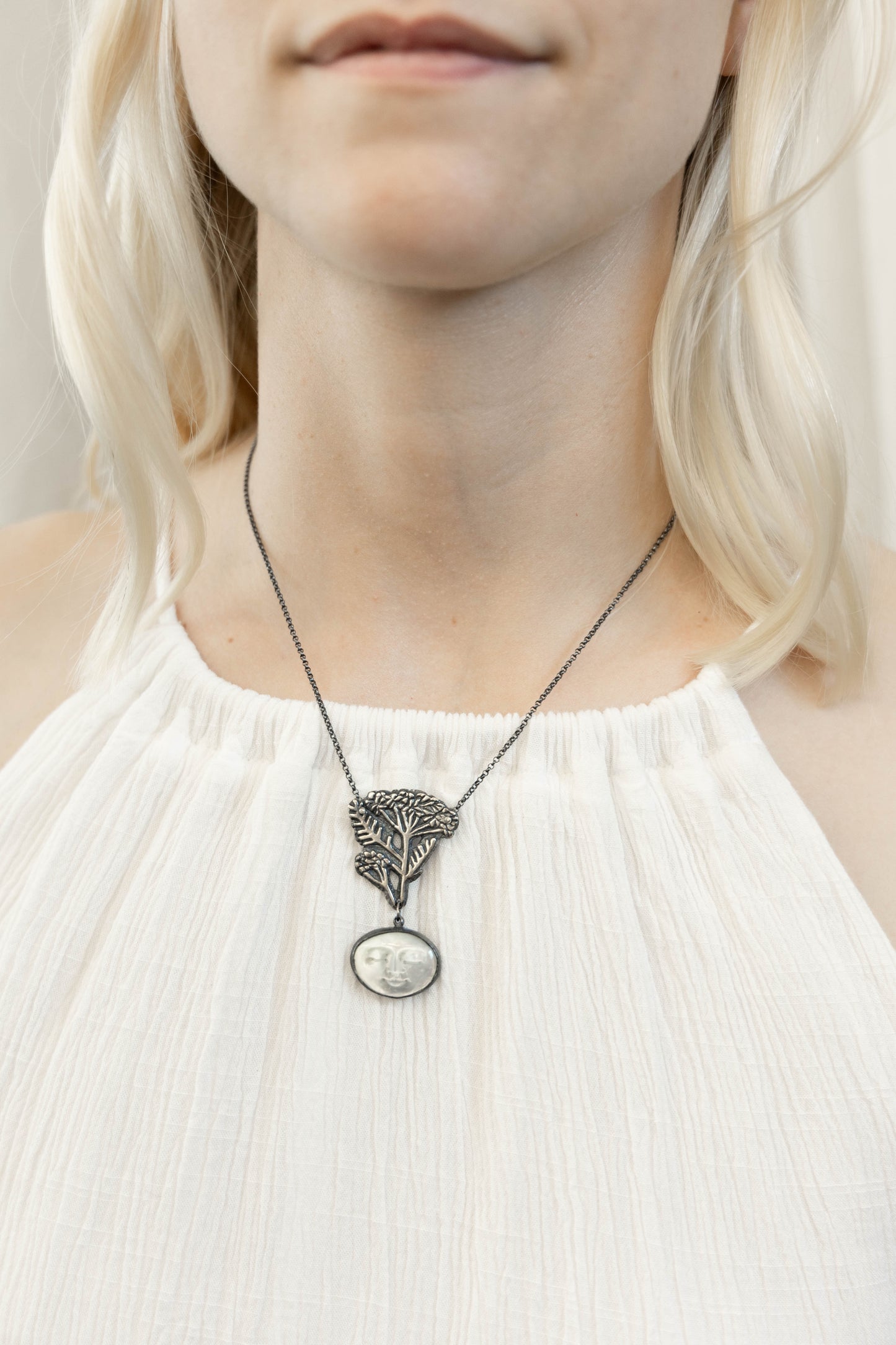 silver necklace with carved mother of pearl moon face and blacked silver yarrow design on a model, by Alice Scott