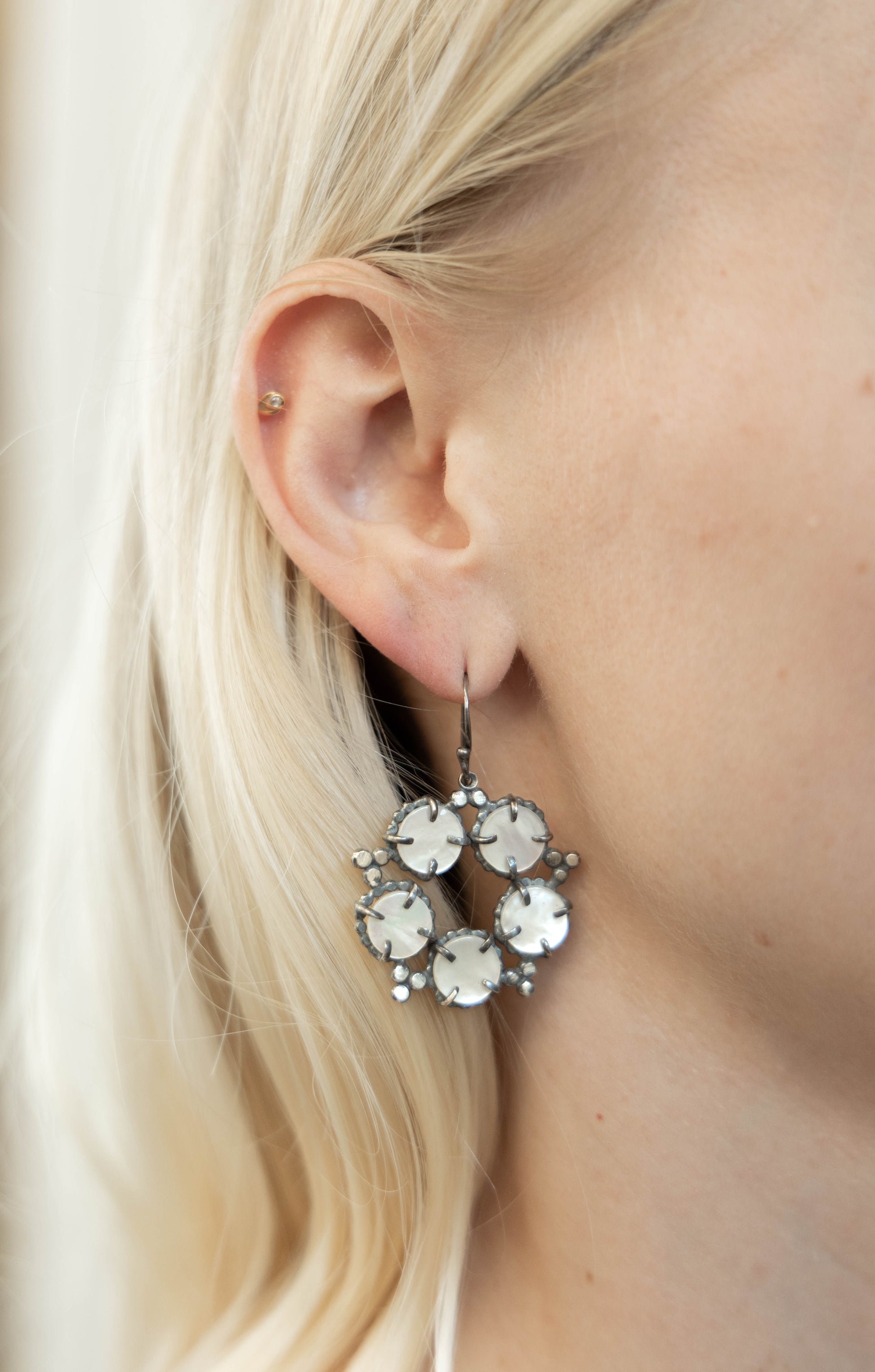 A pair of silver, mother of pearl earrings with a star and constellation design, displayed against a model ear by Alice Scott