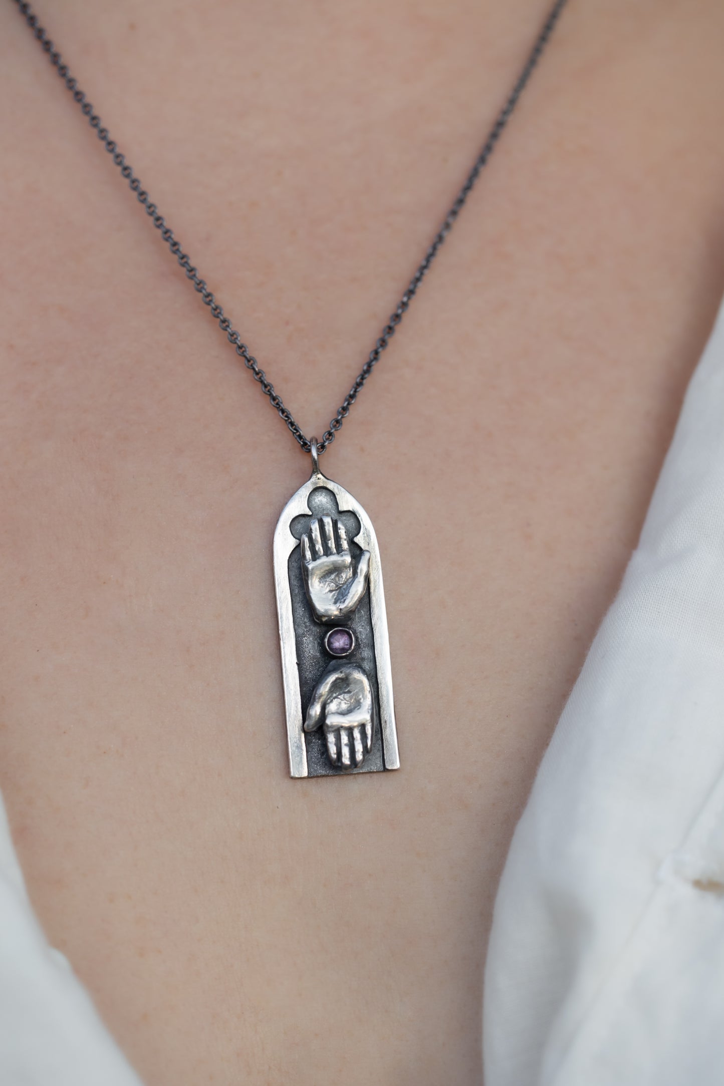 Necklace with a pendant featuring two hands and a purple sapphire on a person's neck.