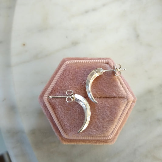 A pair of silver earrings shaped like claws, displayed on a pink hexagonal cushion by Alice Scott