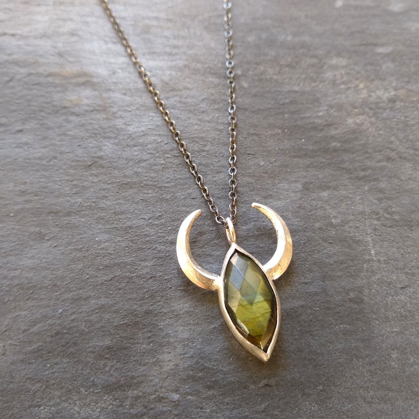 A silver necklace with crescent moon/horn pendant featuring a green labradorite stone by Alice Scott on slate background.