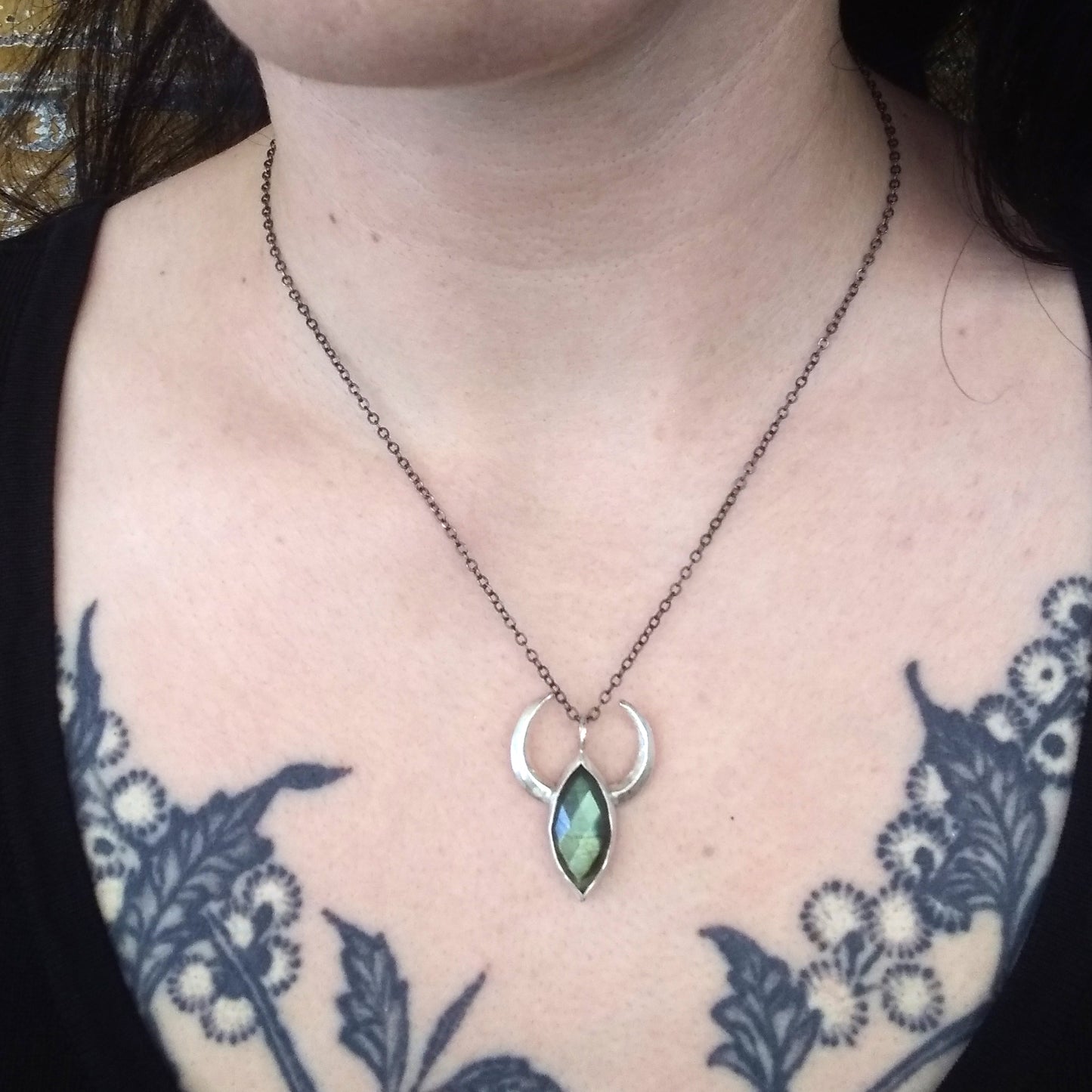 A silver necklace with crescent moon/horn pendant featuring a green labradorite stone by Alice Scott on model neck.