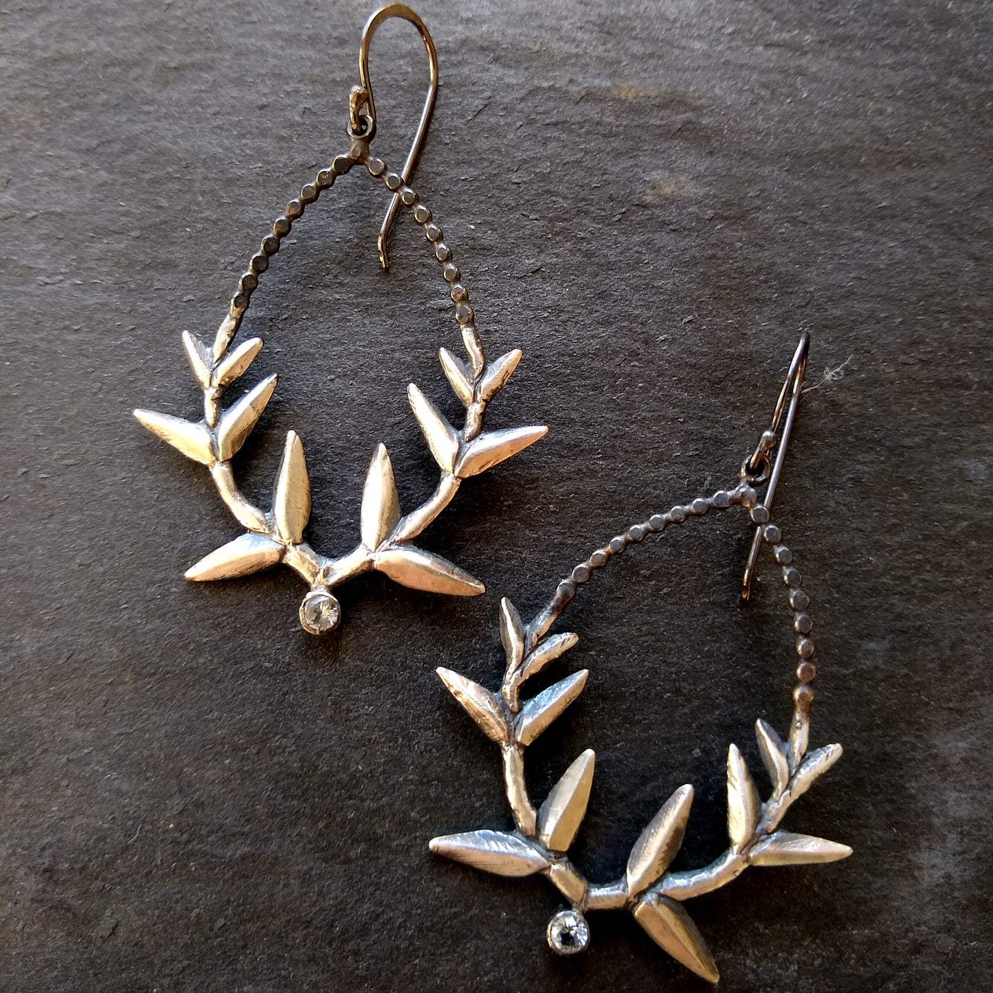 A pair of handmade silver wreath earrings with white topaz accents, displayed against a dark background, by Alice Scott