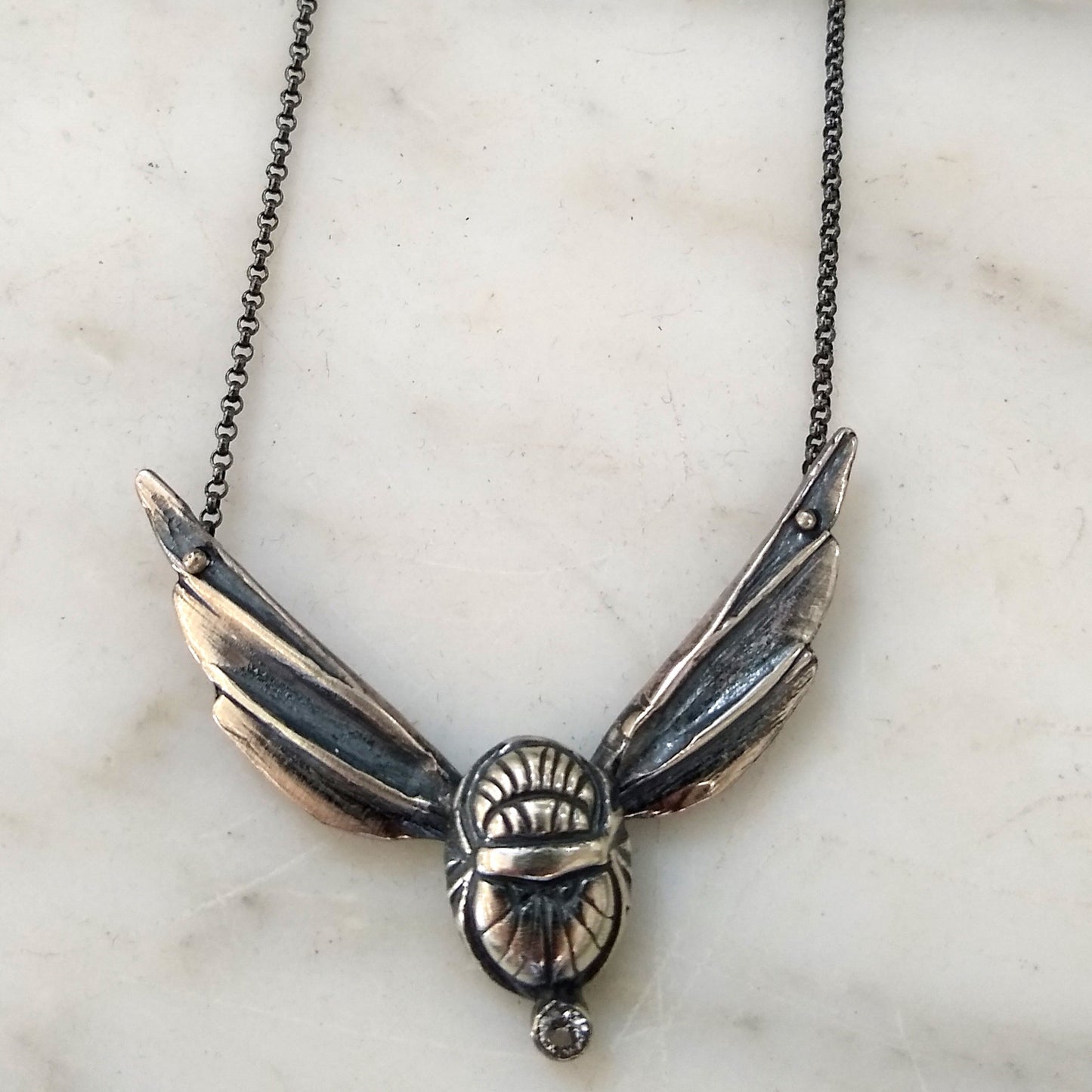 A sterling silver scarab wing necklace with a white topaz stone, displayed on a white background by Alice Scott