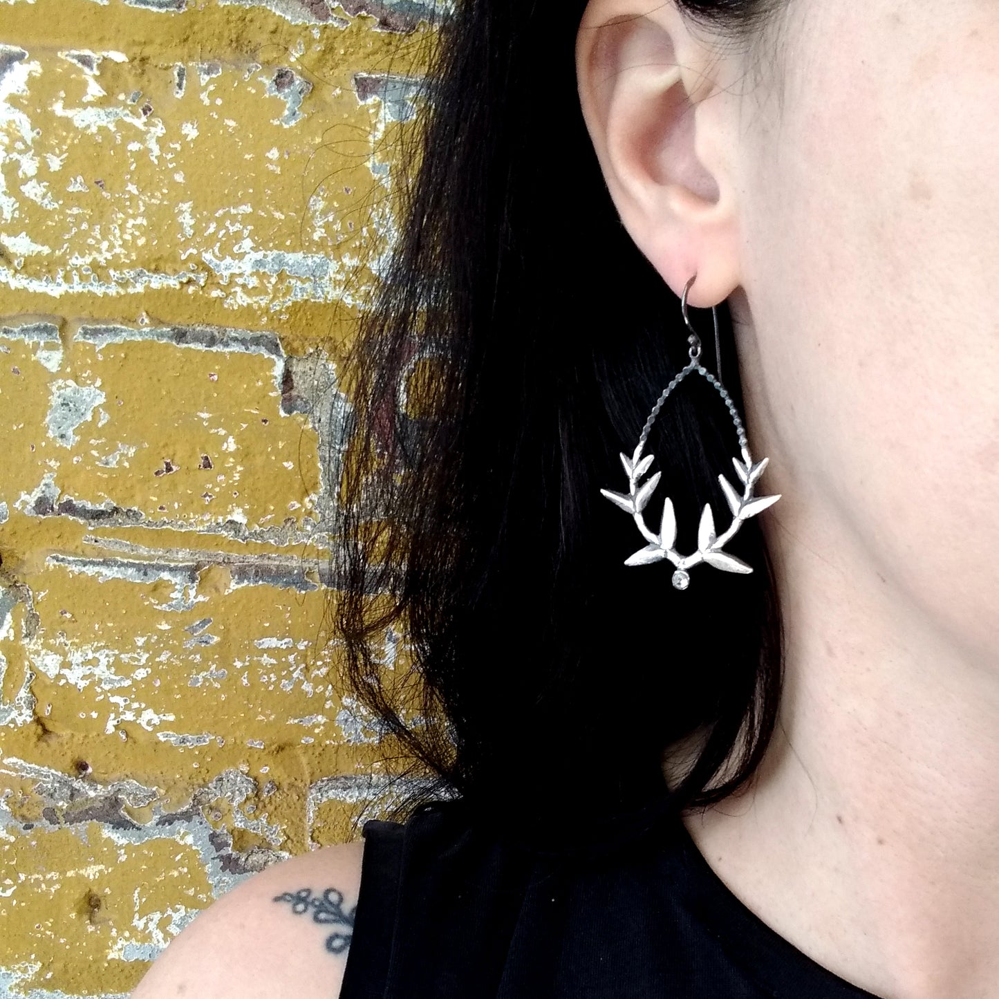 A pair of handmade silver wreath earrings with white topaz accents, displayed against a model ear, by Alice Scott