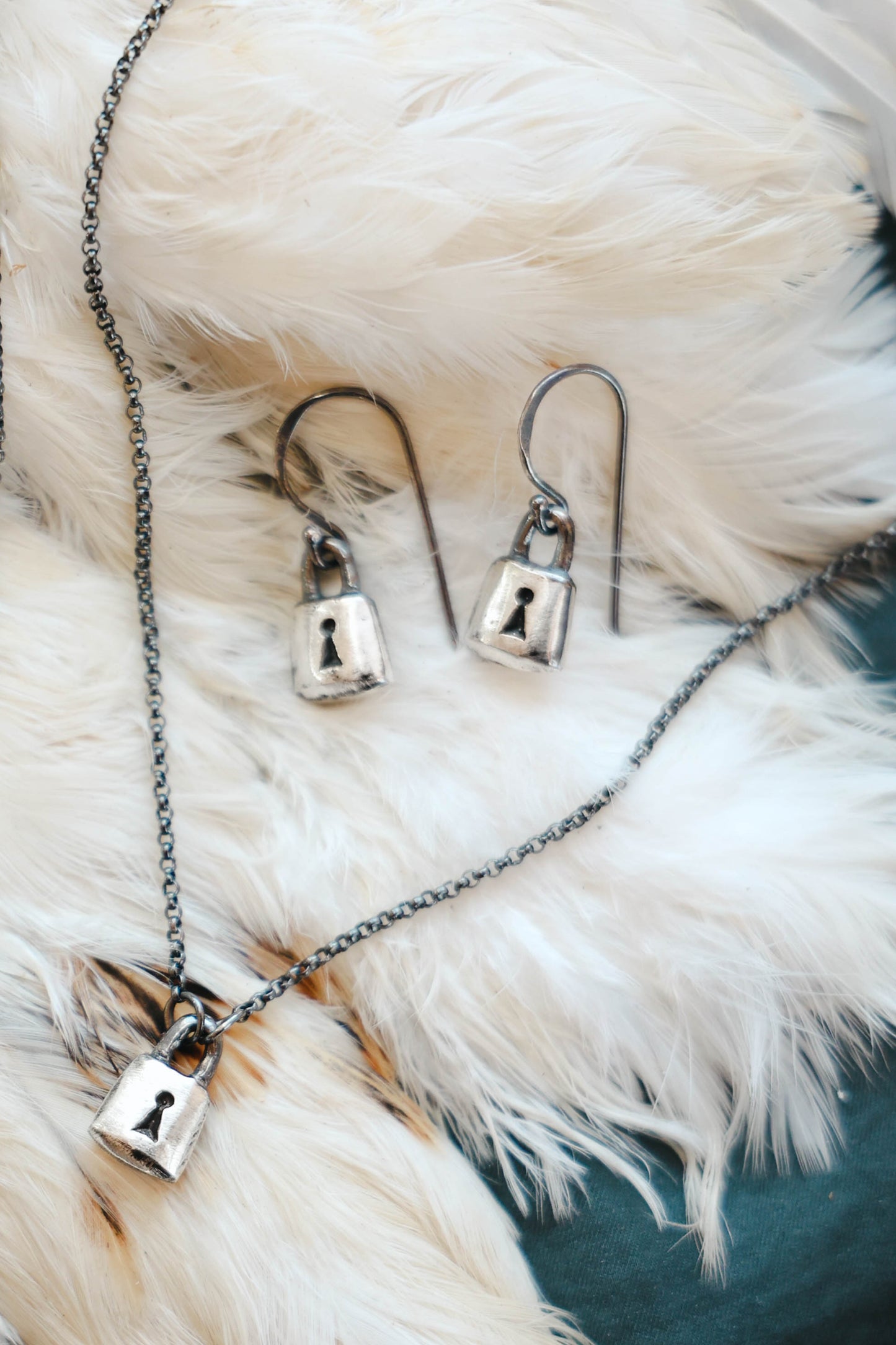 Handmade sterling silver padlock necklace and earrings on black silver chain with feather background and hand, by Alice Scott