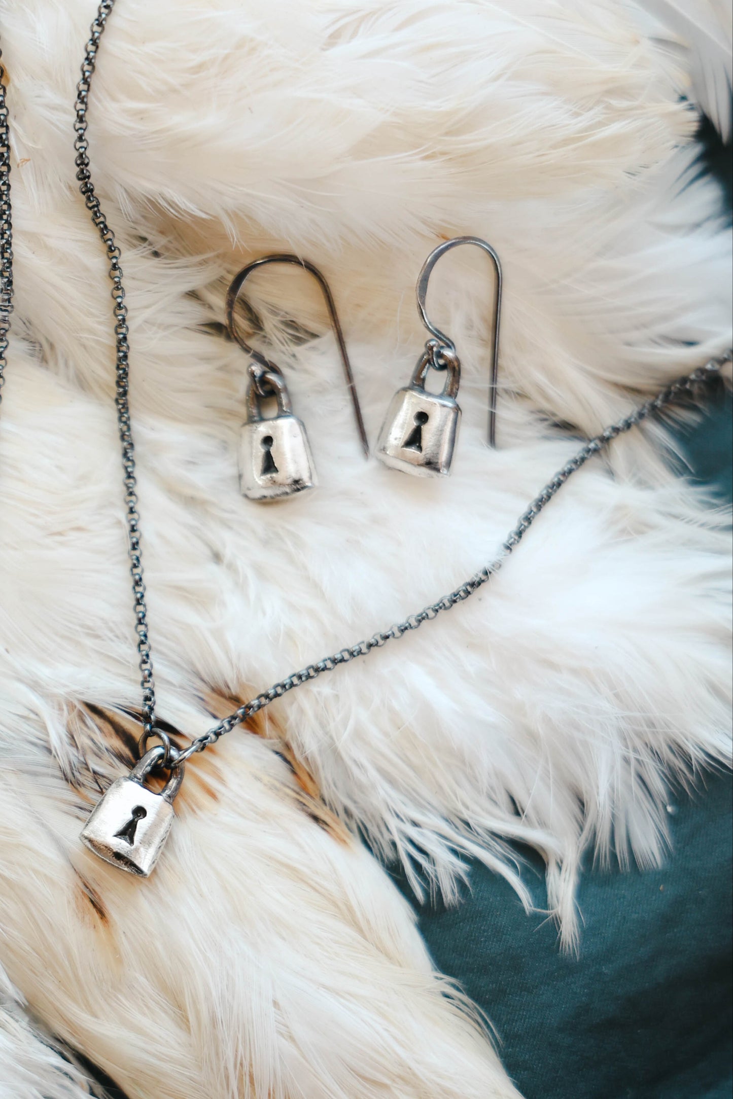 handmade padlock earrings and necklace in sterling silver with black patinas, on feather background by Alice Scott