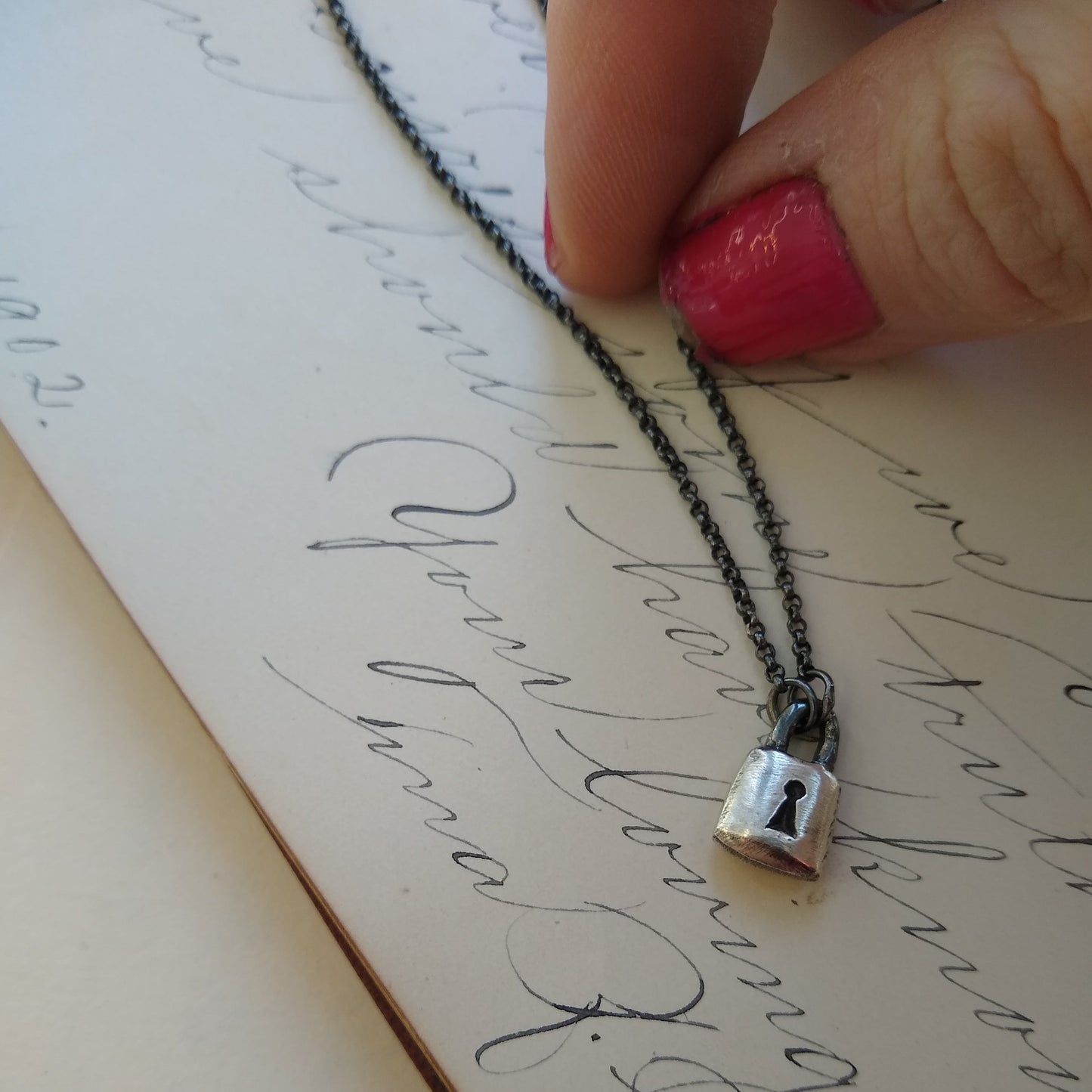 Handmade sterling silver padlock necklace on black silver chain with handwritten note background and hand, by Alice Scott
