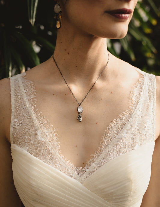 A silver necklace with a rainbow moonstone pendant and a hand talisman charm on a model, by Alice Scott