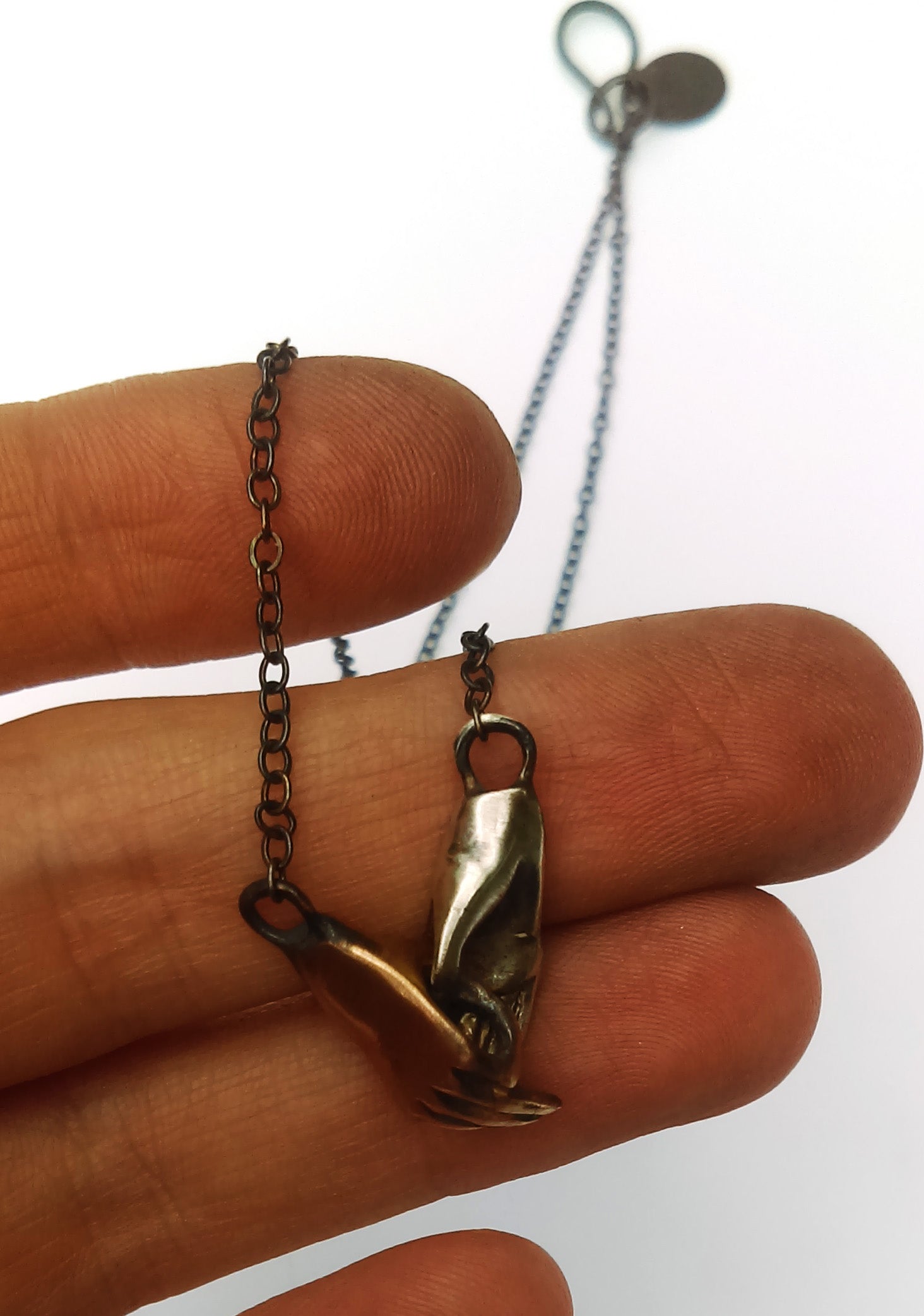 A bronze and silver necklace in the shape of two hands holding each other, displayed against a model hand, by Alice Scott