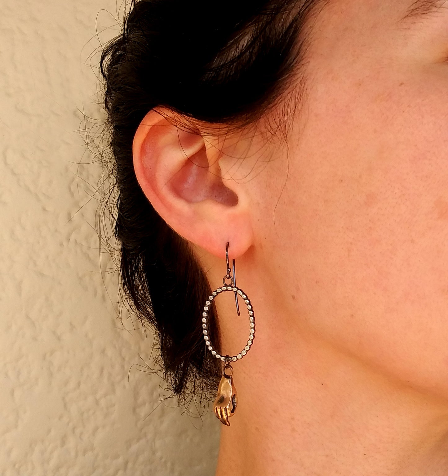 Dotted silver oval earrings with bronze cast meditating hands hanging, by Alice Scott on model ear