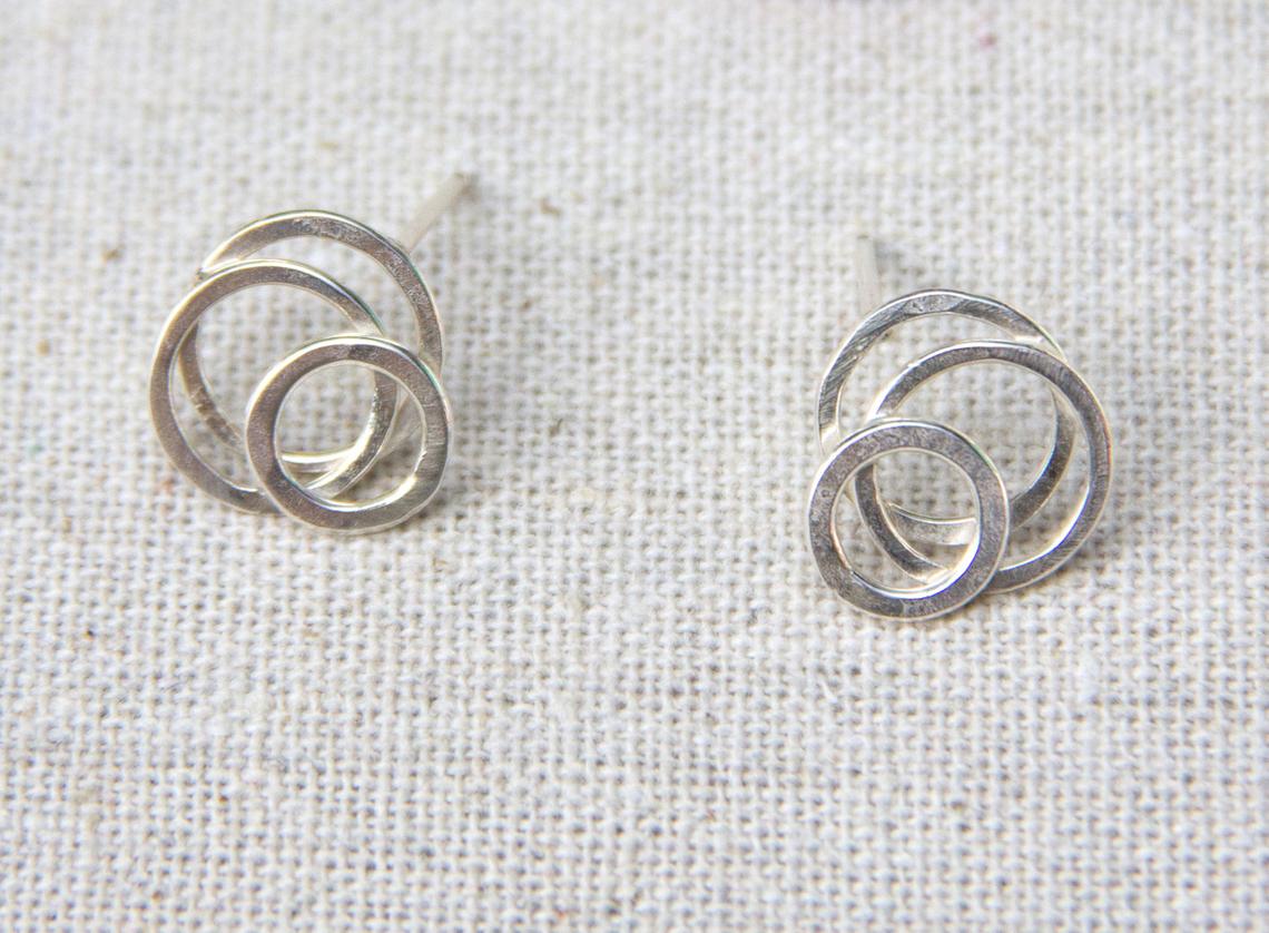 A pair of silver posts with a circular galaxy design, placed on a fabric surface, by Alice Scott