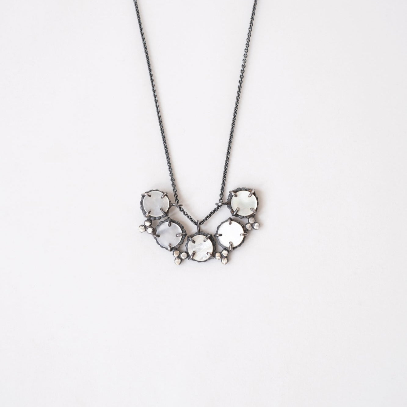 A necklace with a silver chain and a pendant featuring mother of pearl with a star-like pattern, set in black patina sterling silver by Alice Scott