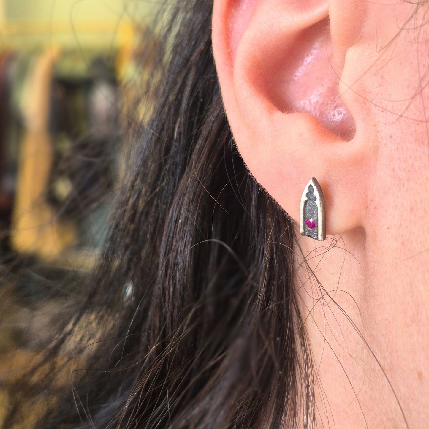 Close-up of an ear wearing a gothic arch earring with rubies by alice scott on a blurred background