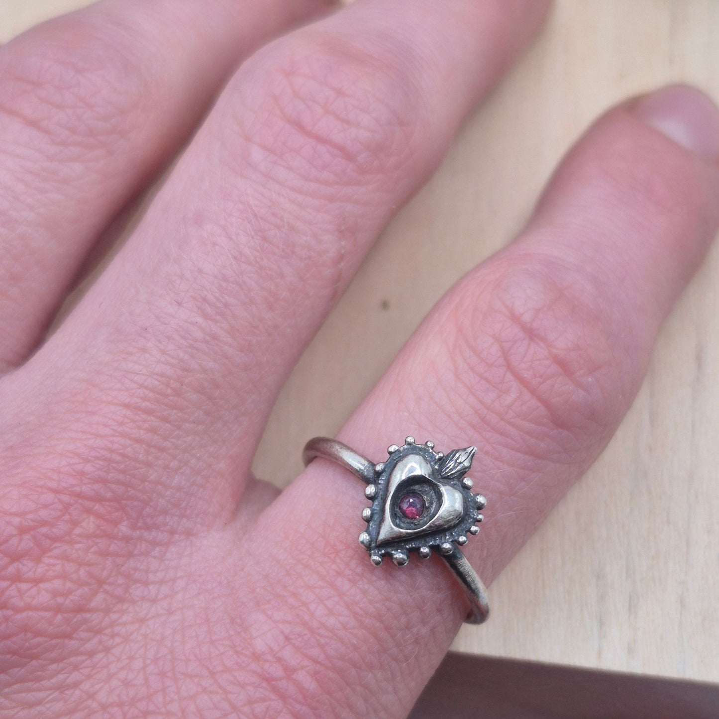 Silver ring with a heart-shaped gemstone on a finger against a neutral background by Alice Scott