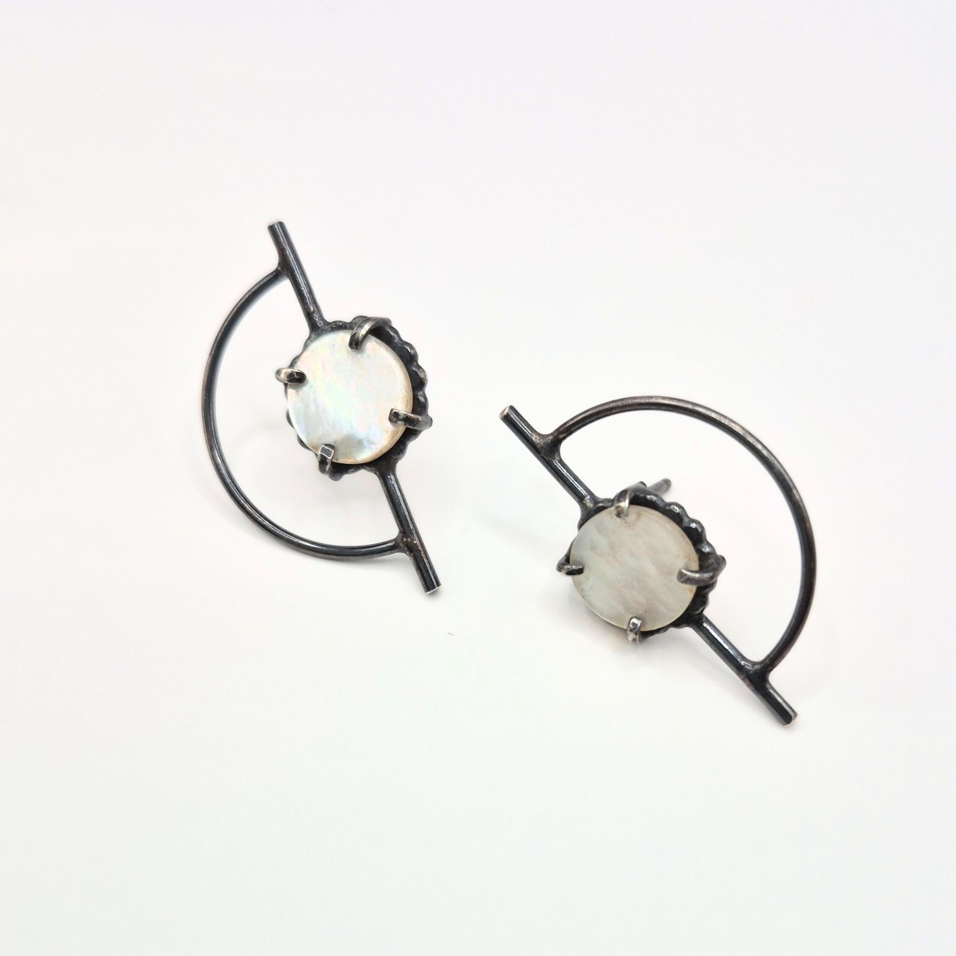 A pair of Orbit posts earrings with mother of pearl, featuring a geometric design with black silver posts and white-colored mother of pearl circles by Alice Scott