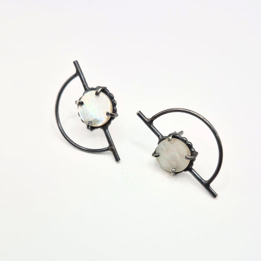 A pair of Orbit posts earrings with mother of pearl, featuring a geometric design with black silver posts and white-colored mother of pearl circles by Alice Scott