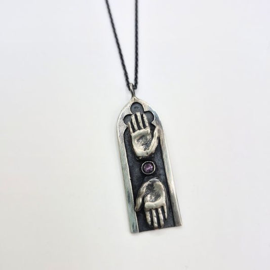 Silver pendant with two hands design with purple on a white background by Alice Scott