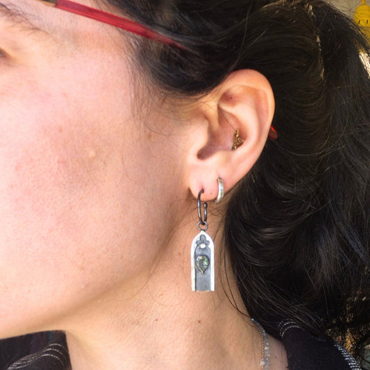 Close-up of an ear with a silver gothic arch earring featuring a green moss agate stone and white sapphire, by Alice Scott.