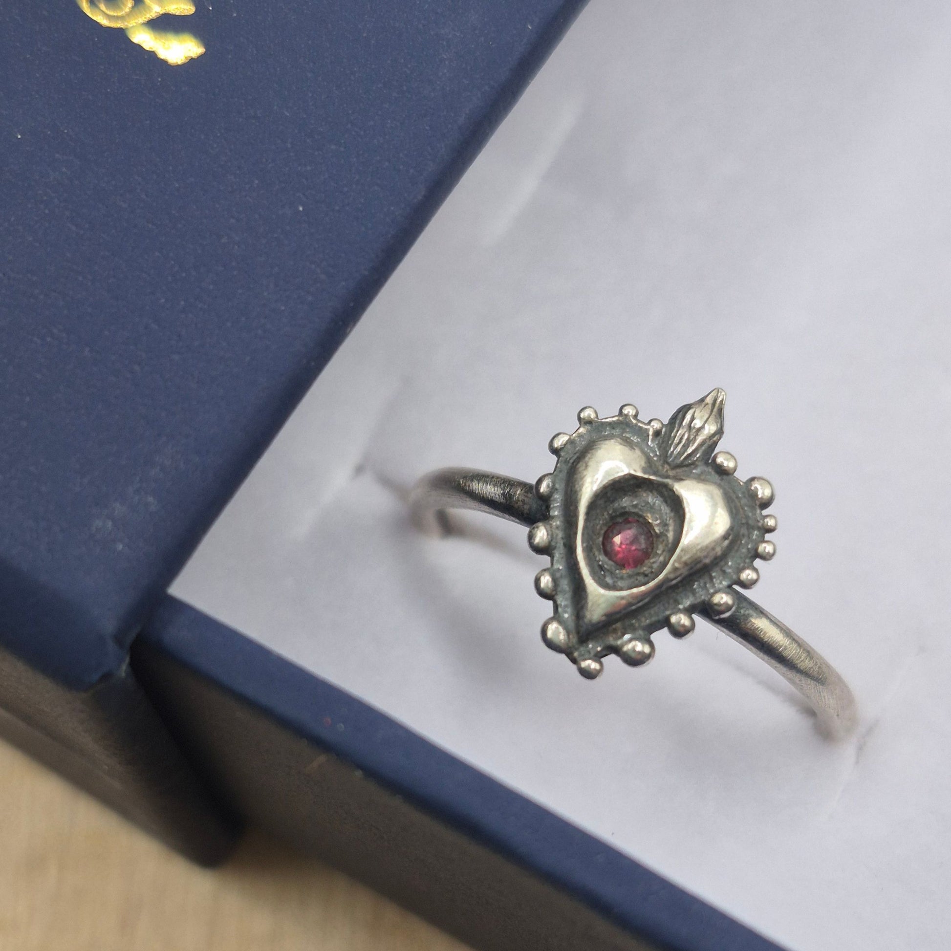Silver heart-shaped ring with a red  ruby gemstone on a white surface by Alice Scott