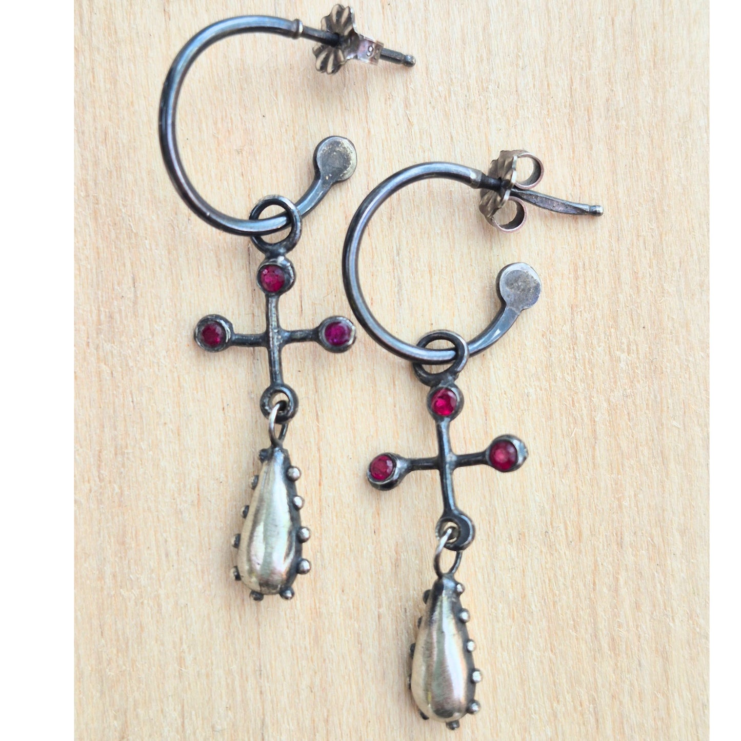 Pair of ornate earrings with ruby gemstones on a wooden surface by Alice Scott