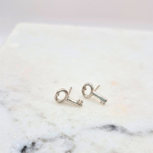 A pair of sterling silver key-shaped earrings placed on a marble surface by Alice Scott