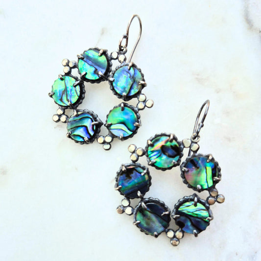 A pair of blue abalone earrings with sterling silver settings, arranged in a constellation pattern on a white marble surface by Alice Scott