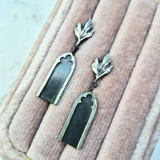 A pair of sterling silver earrings designed as gothic archways with leaf details, displayed on a pink velvet surface by Alice Scott