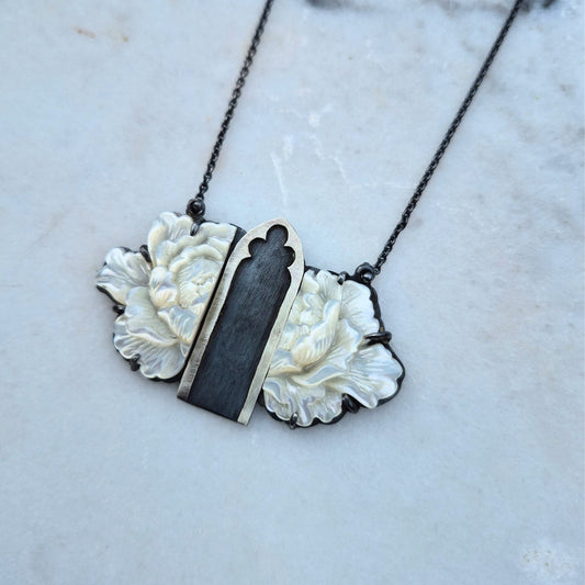 A necklace with a mother of pearl flower design and Gothic archway cutouts, silver necklace on marble background by Alice Scott
