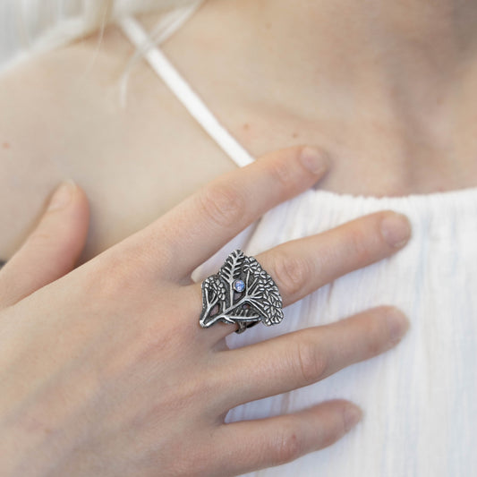Silver ring with a  yarrow herb design and sapphire worn on a finger, against a white background, ring made by Alice Scott