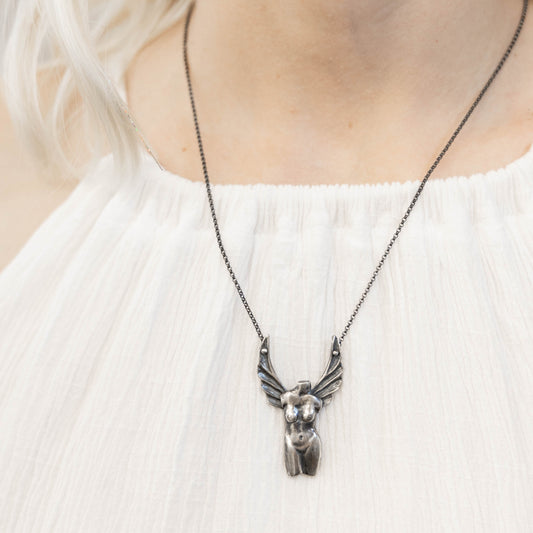 A silver necklace with a detailed pendant representing the Winged Venus figure, suspended on a black patina chain on a model neck, by Alice Scott