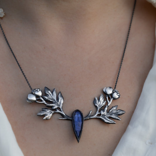 Necklace with carved hawthorn branch design and blue labradorite stone worn by a person by Alice Scott