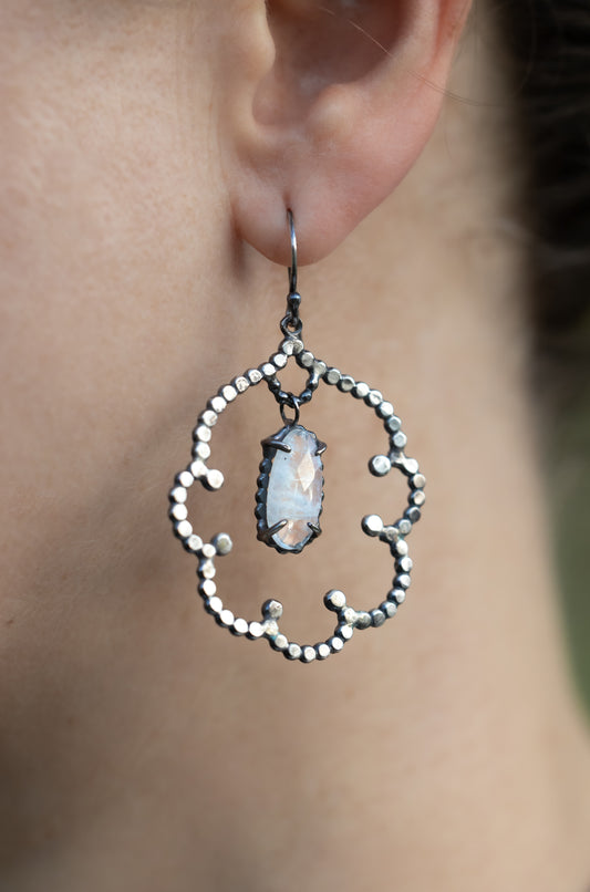 Close-up of an ornate silver earring with a central moonstone gemstone worn by a person, by Alice Scott