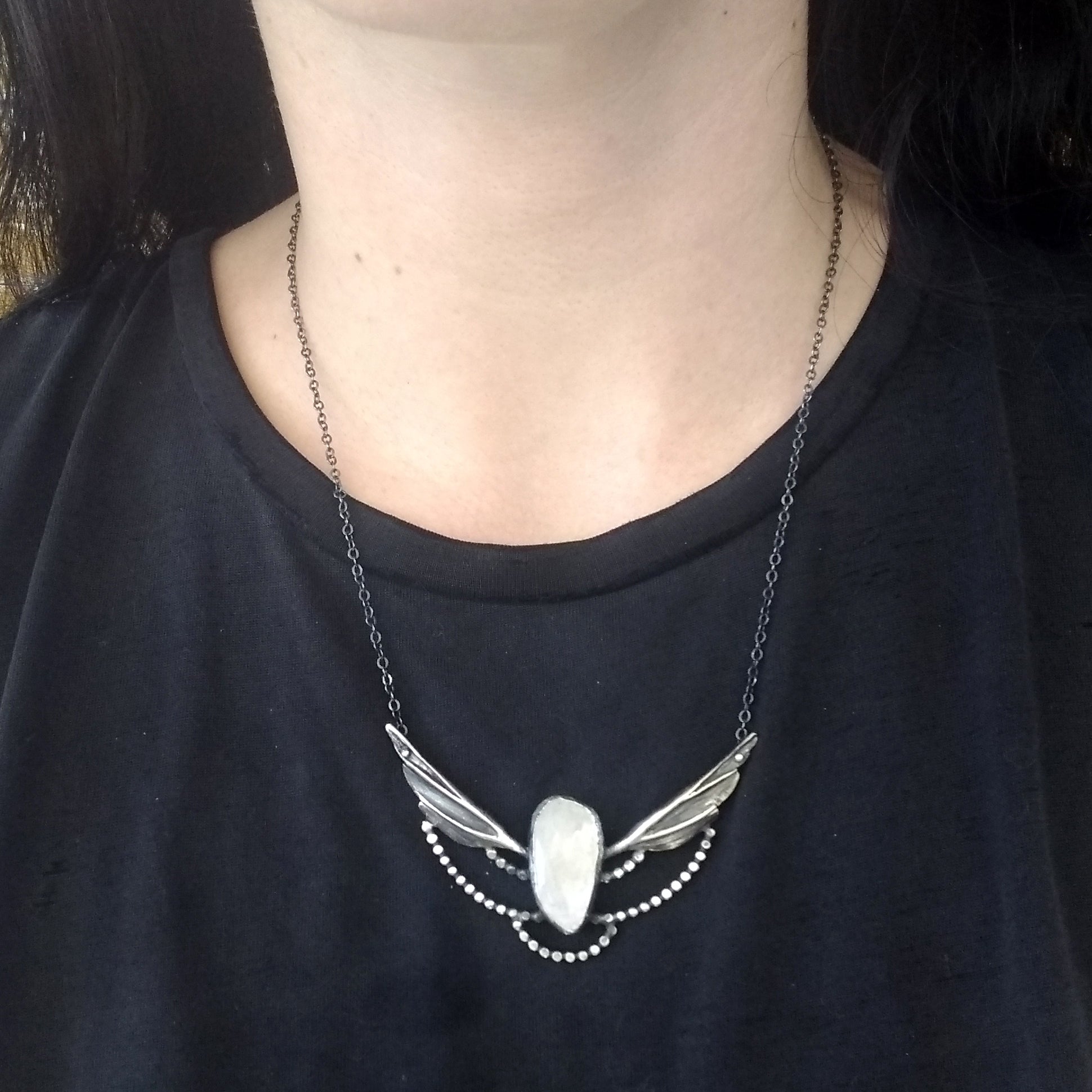A silver necklace with a moonstone wing pendant and small silver accents on a model neck by Alice Scott