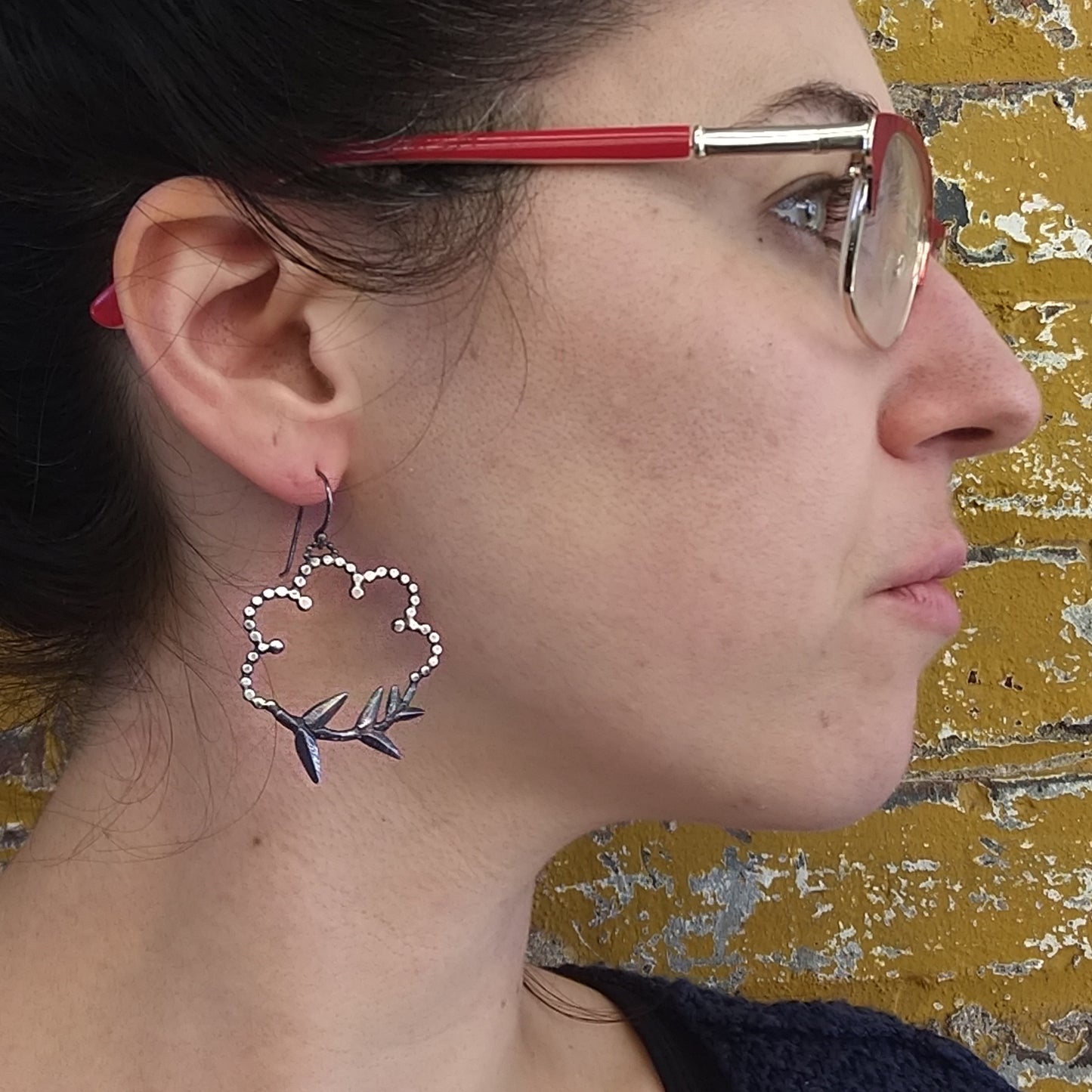 A pair of silver earrings designed with root and cloud motifs, displayed on a model ear, by Alice Scott.